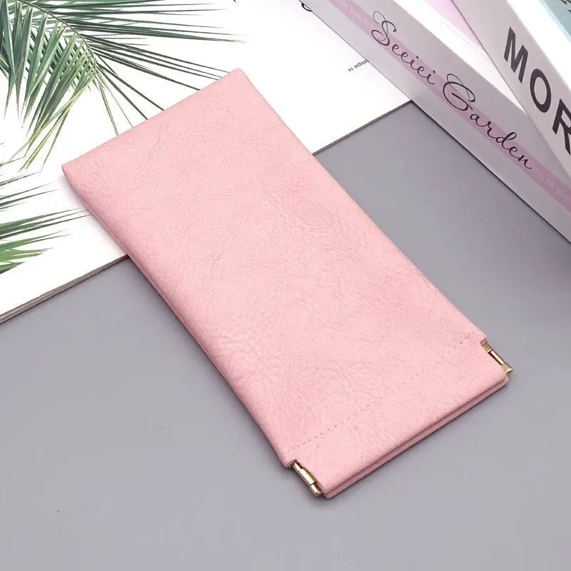 A pink premium PU leather eyewear storage bag lying on a gray surface next to some books.
