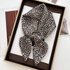 A luxury leopard print silk scarf tied in a bow displayed in a dark wooden box.