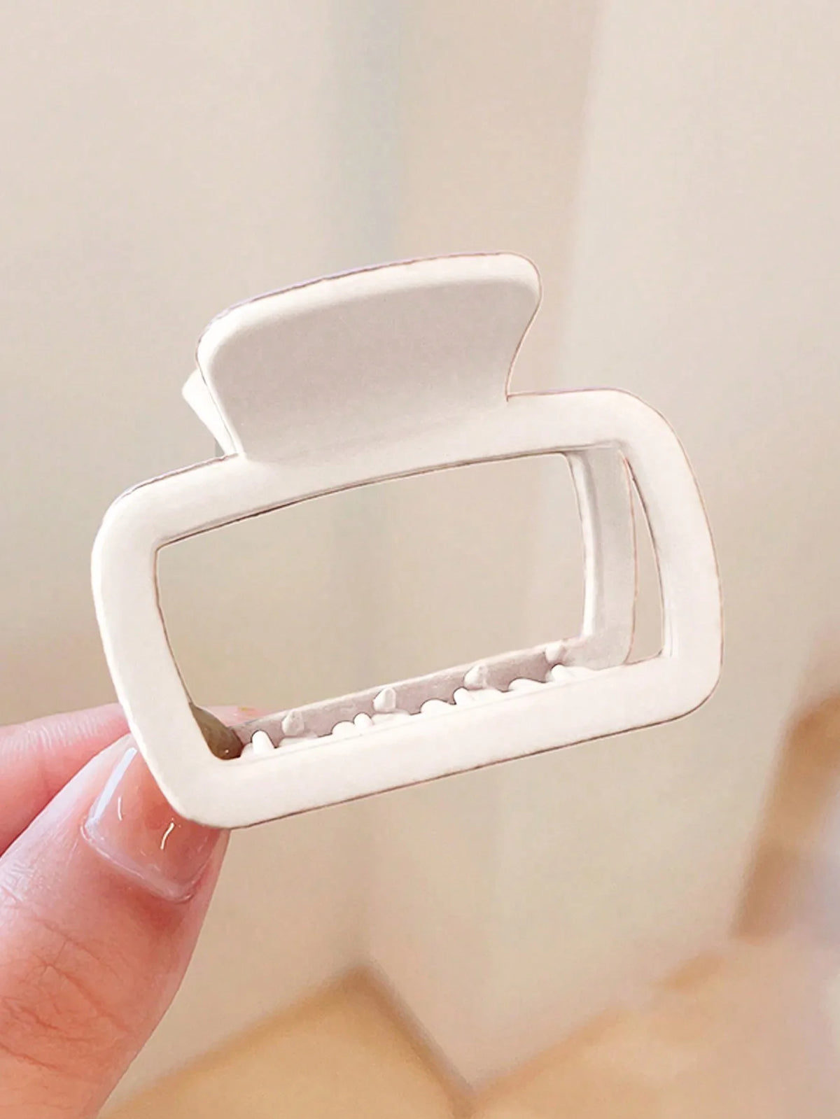 A white square lightweight hair claw clip is held by a hand against a light background.