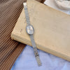 Une montre en quartz argentée avec un bracelet métallique repose sur un vieux livre à côté d'une surface en bois.