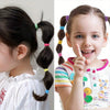A young girl with brown hair styled in pigtails secured with colorful elastic hair bands.