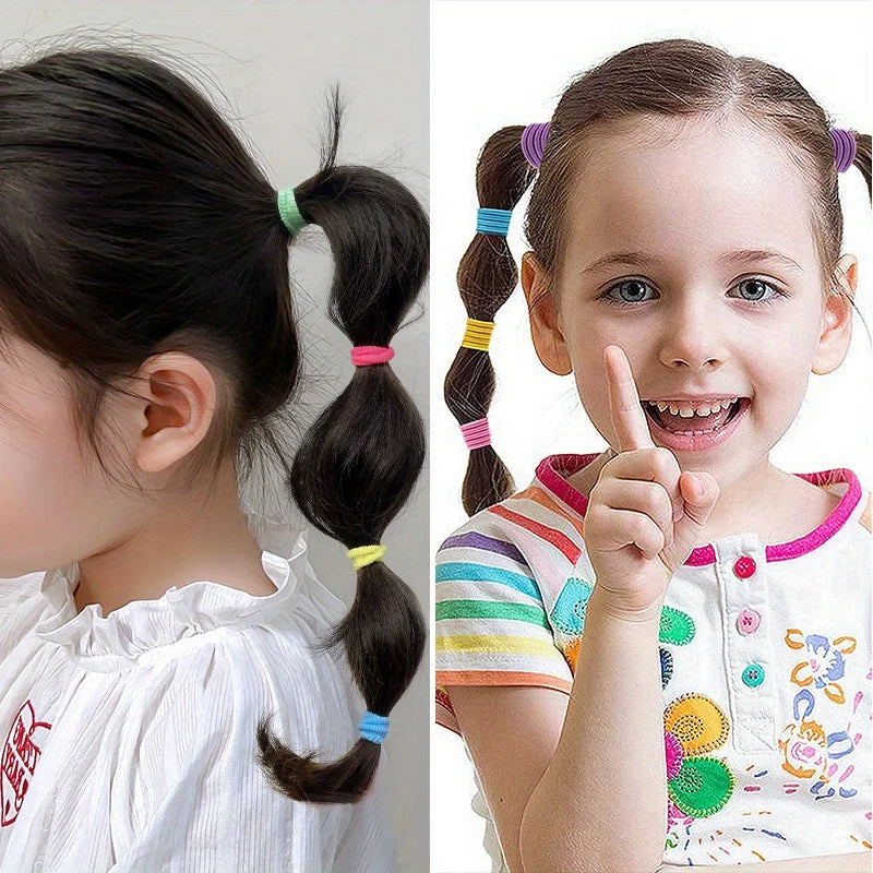 A young girl with brown hair styled in pigtails secured with colorful elastic hair bands.