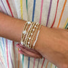 Un poignet portant une pile de bracelets perlés en perles dorées contre un vêtement rayé.