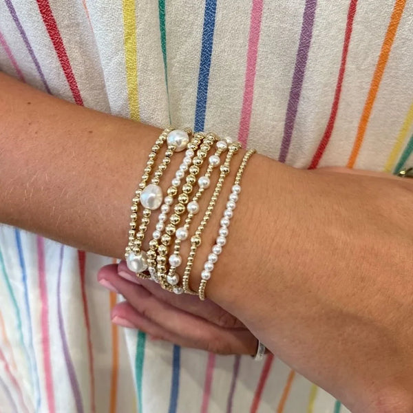 A wrist wearing a stack of multiple gold-plated pearl beaded bracelets against a striped garment.