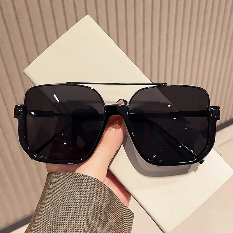 A pair of black double bridge oversized square sunglasses resting on a white surface.