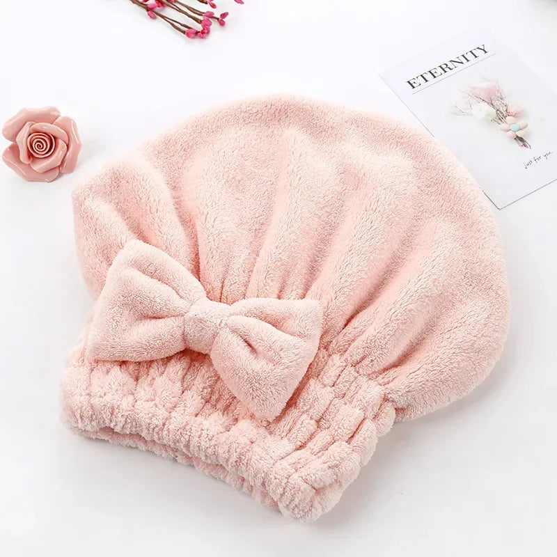 A soft pink microfiber hair drying towel with a pom-pom detail is displayed on a white background.