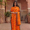 A woman wearing an orange floral print satin maxi shawl standing in a terracotta-colored architectural setting.