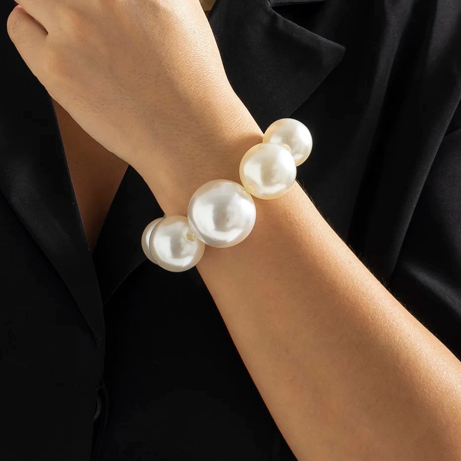 Un poignet portant une guirlande de perles blanches imitations sur une manche noire.