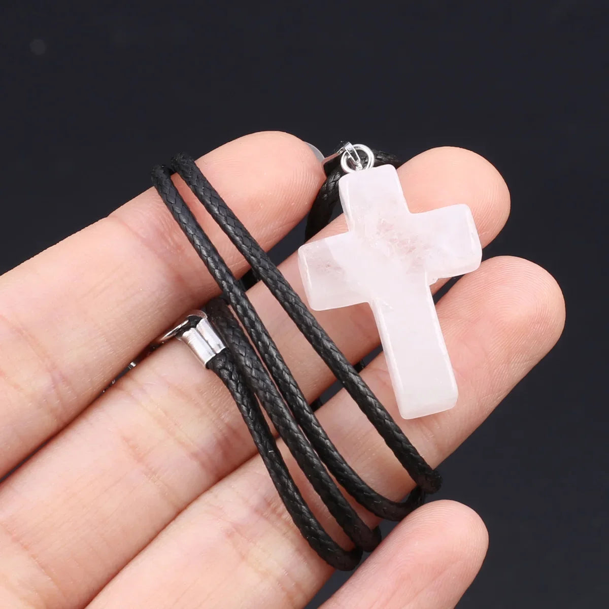 Ein durchsichtiger rosa Tigerauge-Agat-Kreuz-Anhänger-Halskette wird von einer Hand gehalten.