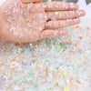 A hand displays a set of 10 pink and white resin nail art charms scattered across the skin.