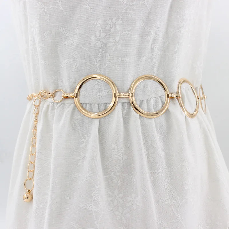 Cinturón de cadena metálica dorada de moda usado sobre un vestido blanco.