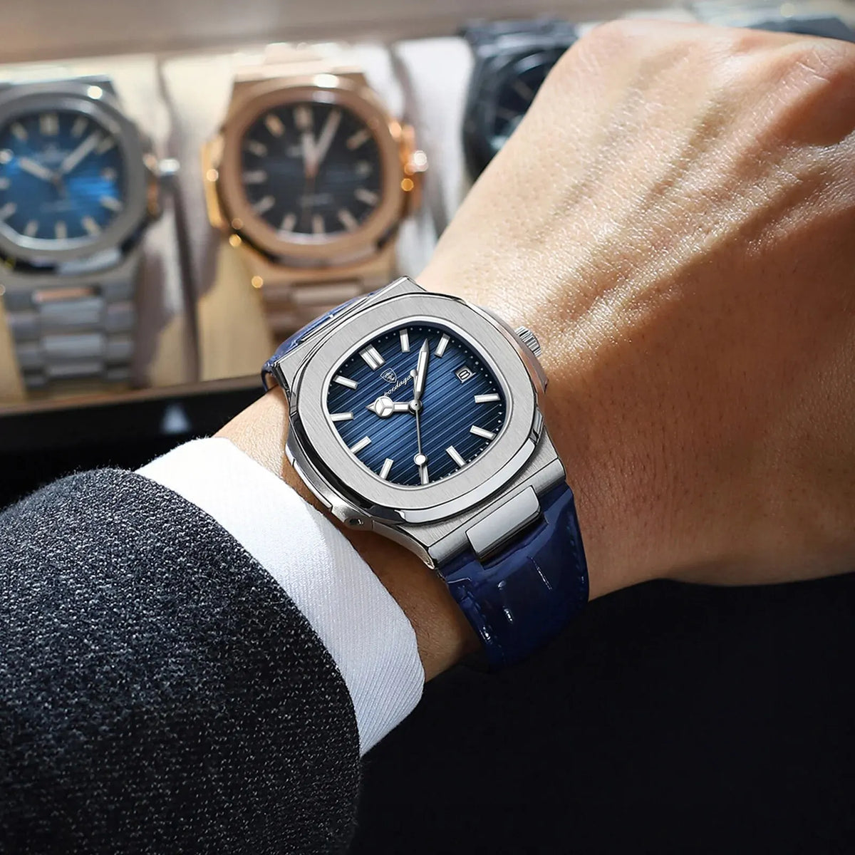 A close-up of a blue and silver luxury square men's watch with a dark blue strap on a wrist.