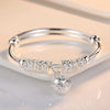 A silver bell bangle bracelet with intricate filigree detailing and a dangling charm resting on a white surface.