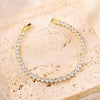 A gold-toned stacking bracelet set featuring a continuous line of clear rhinestones on a light pink stone surface.