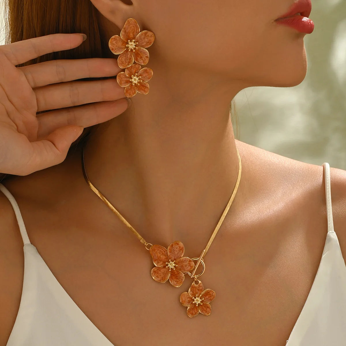 A close-up of a woman wearing a gold floral pendant necklace and matching earrings against her neck and face.