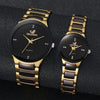 A pair of gold-toned analog quartz watches with black faces and straps displayed on a dark surface.