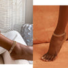 A close-up of a woman's ankle wearing gold plated minimalist Cuban link anklets against an orange background.