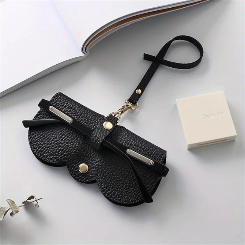 Black PU leather eyewear pouch and glasses case with a black strap resting on a white surface.