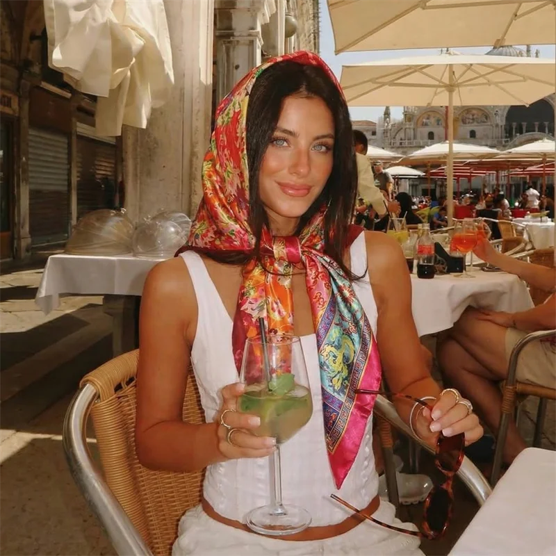 Eine Frau trägt einen farbenfrohen Seidensatin-Hijab und sitzt an einem Café-Tisch im Freien.