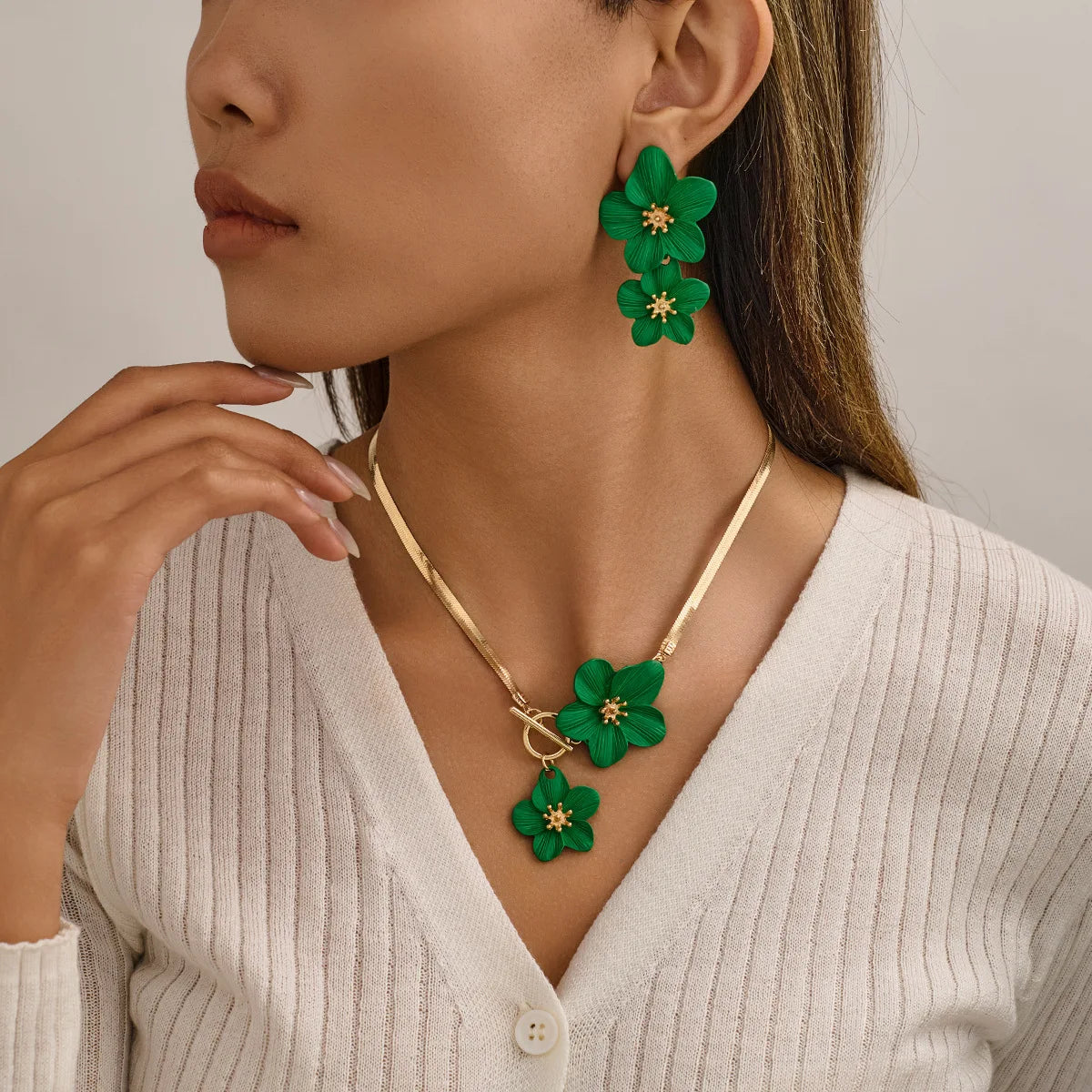A close-up of a woman wearing a gold floral pendant necklace and matching earrings against a light sweater.