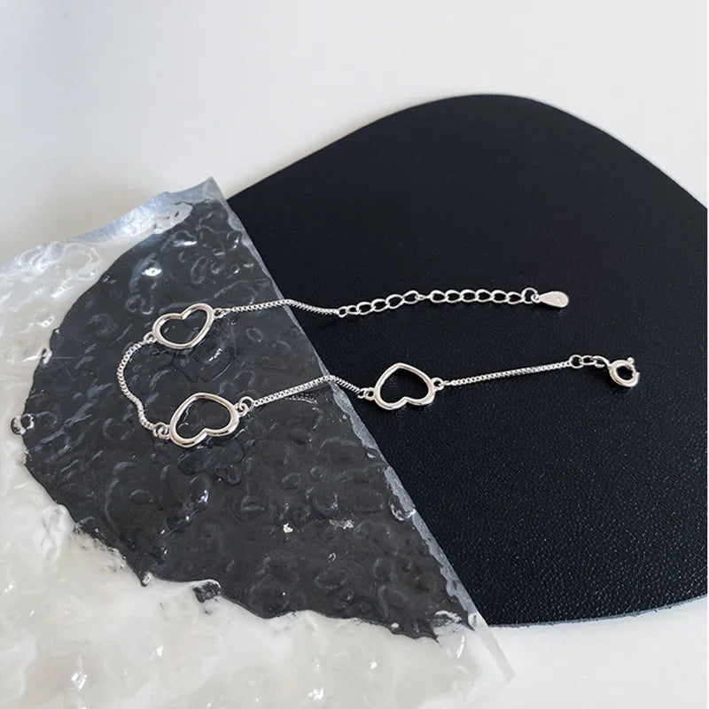 Sterling silver double heart charm bracelet displayed on a black surface next to a piece of rough, translucent stone.