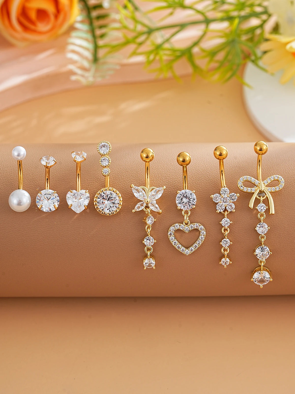 A set of gold dangle curved belly piercing jewelry featuring heart and flower designs.