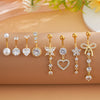 A set of gold dangle curved belly piercing jewelry featuring heart and flower designs.