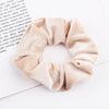 A beige velvet scrunchie is shown against a white background, resting on a piece of paper.