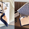 A silk scarf featuring a navy and beige chevron pattern with small pink polka dots, displayed on a white card.