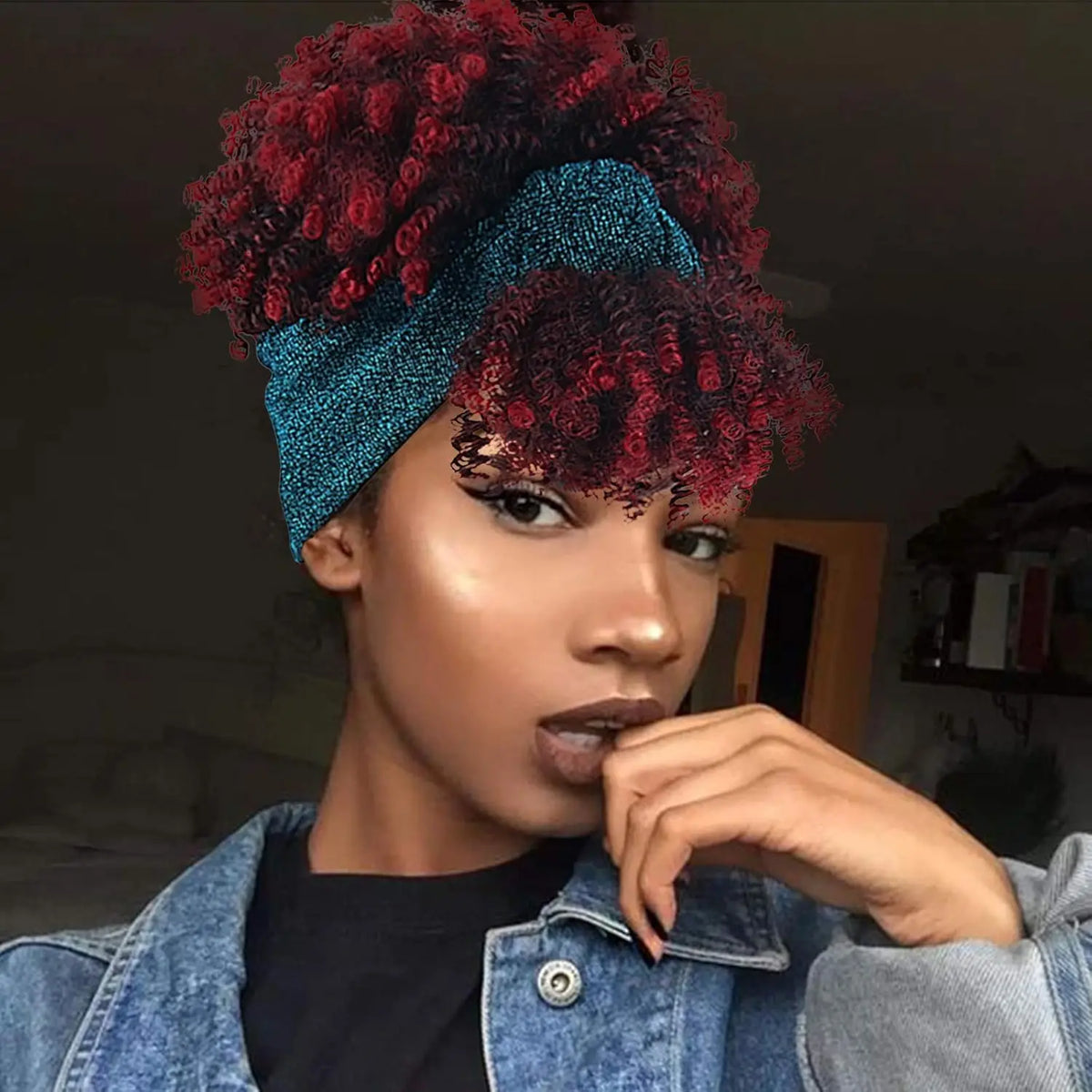 Una mujer vistiendo una peluca afro rizada roja vibrante con una diadema azul y una chaqueta de mezclilla.