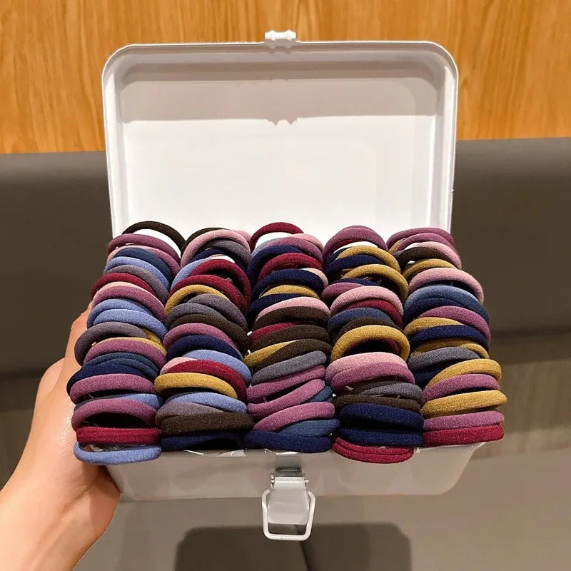 Eine Hand hält eine offene, klare Box mit farbenfrohen elastischen Haargummis für Zöpfe und Pferdeschwänze.