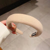 Un bandeau pour cheveux beige épaissi, tenu, affichant le nom de la marque sur le bord intérieur.