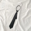 A black clip-on tie is laid diagonally on a white fabric background.