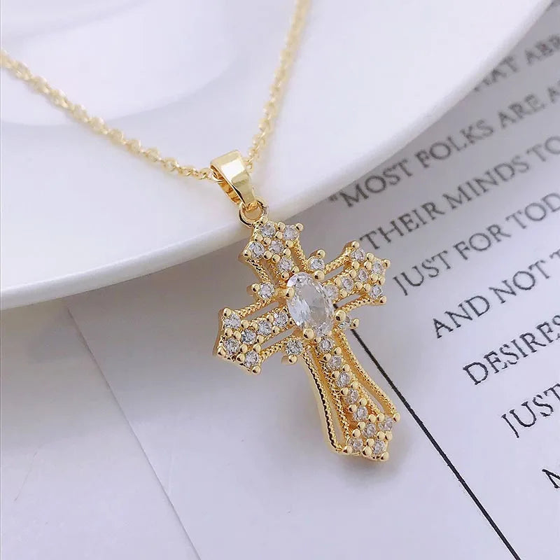 A dainty gold cross charm necklace with clear stones is displayed on a white background.