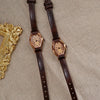 Un par de relojes de cinturón de cuero marrón retro con detalles dorados y pedrería sobre tela beige.