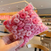A hand holds a clear plastic package of pink fluffy elastic hair bands for girls.