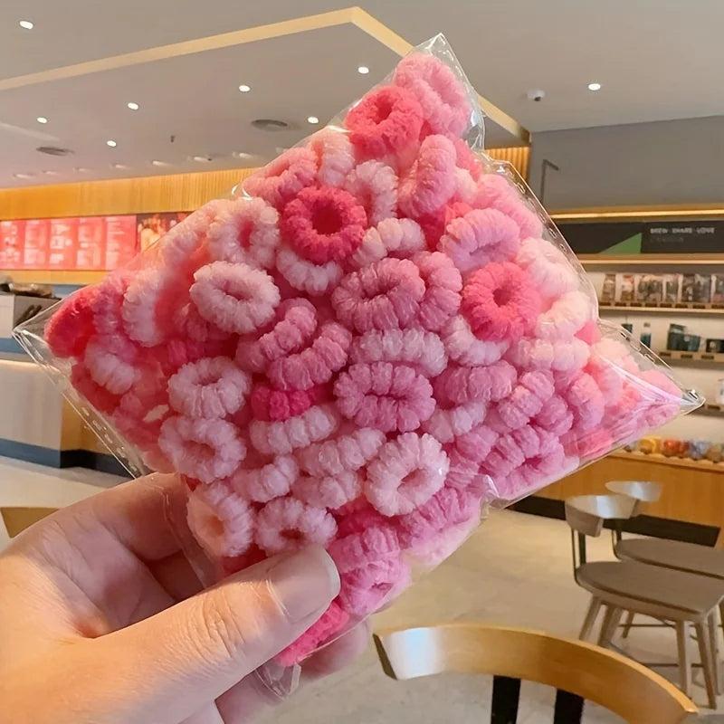 A hand holds a clear plastic package of pink fluffy elastic hair bands for girls.