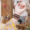 A hand wearing a striped bracelet holds a textured fabric, with boho hair ties and headbands visible in the background.