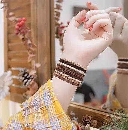 A hand wearing a striped bracelet holds a textured fabric, with boho hair ties and headbands visible in the background.