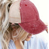A close-up of a vintage mesh baseball cap in maroon and beige colors worn by a blonde woman.