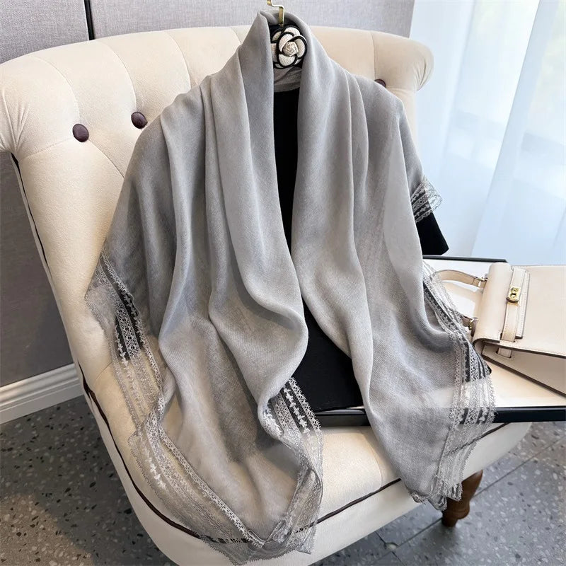 A gray shawl with bohemian lace trim draped over a white armchair.