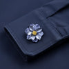 A dark blue fabric button cover featuring a pressed, silvery-blue flower with a gold center.