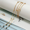 Collares de gafas con perlas y cuentas tono dorado colgados sobre un fondo blanco.
