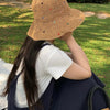 Una mujer lleva un sombrero de paja panamá tejido a mano, sentada al aire libre en un área de césped.