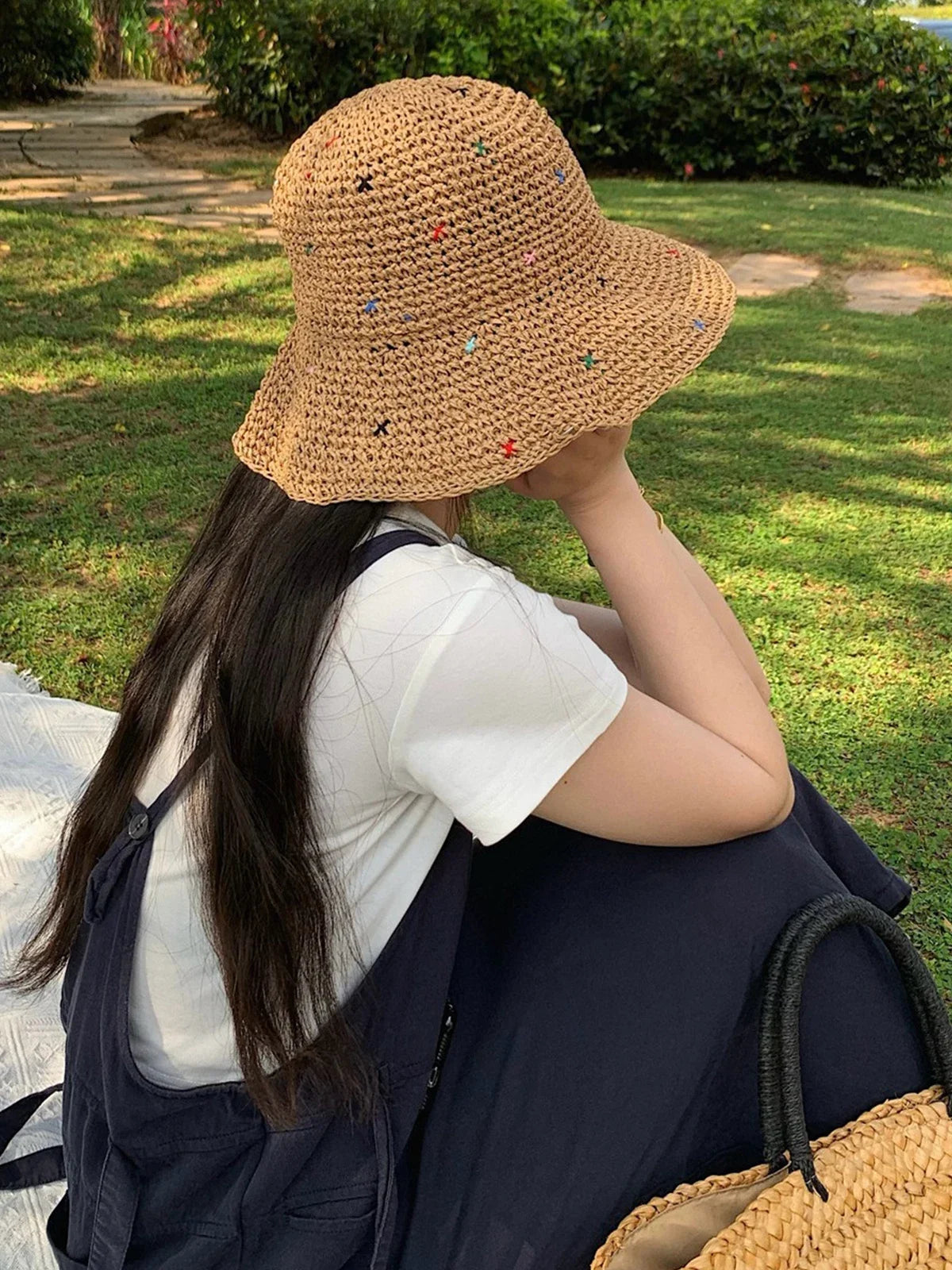 Una mujer lleva un sombrero de paja panamá tejido a mano, sentada al aire libre en un área de césped.