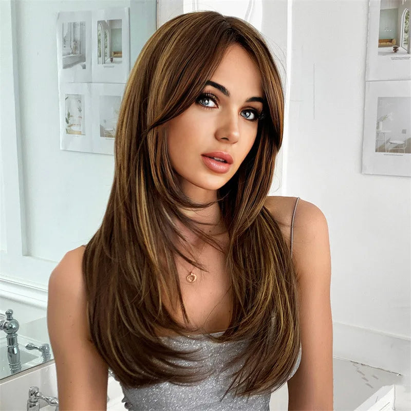 A woman modeling a long brown wig with subtle highlights in a natural indoor setting.