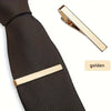 A close-up of a black textured tie with a gold metal tie clip.