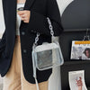 Una persona vistiendo un blazer negro y pantalones color arena sostiene un bolso cruz transparente con cadena de plata.