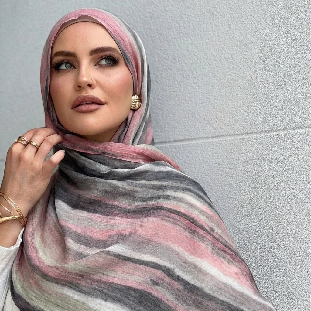 Una mujer vistiendo un pañuelo hiyab a rayas rosa y gris mirando directamente a la cámara.
