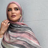 Una mujer vistiendo un pañuelo de hijab a rayas rosa y gris mirando directamente a la cámara.